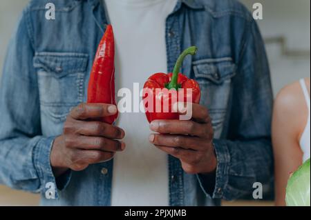 dark-skinned man holding red sweet pepper. Close-up of red pepper in hands. Stock Photo