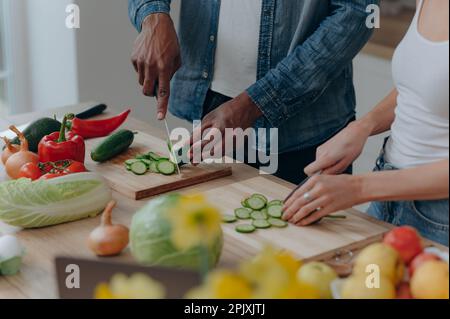 Close up of a cutting board with the hands of a couple cutting vegetables together in the kitchen. Vegetarian healthy food Stock Photo