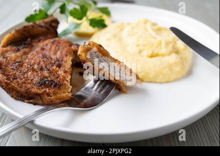 Italian breaded pork chop with parmesan cheese. Served with fresh polenta on a plate Stock Photo