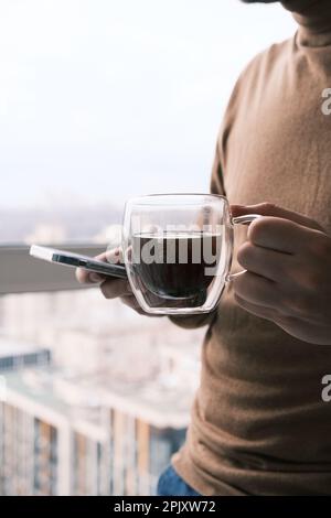 businessman drinking coffee, looking in smartphone with background window at big modern city, having break, deep in thoughts, enjoying view, waiting Stock Photo