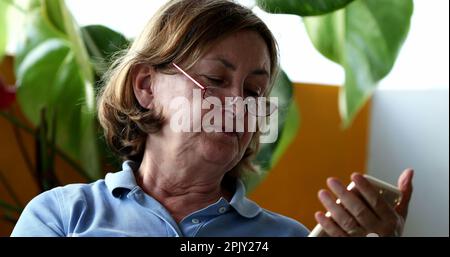 Older woman reading out loud holding cellphone, senior person looking at screen reading Stock Photo