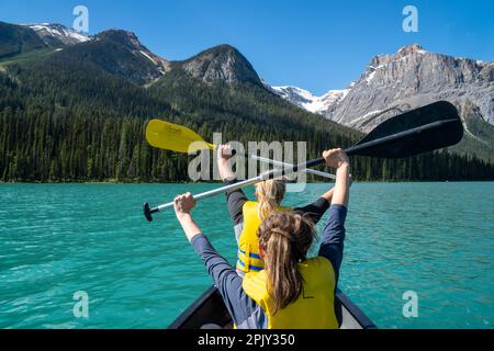 Two woman hold up paddle oars while canoeing on Emerald Lake in the Canadian Rockies Stock Photo
