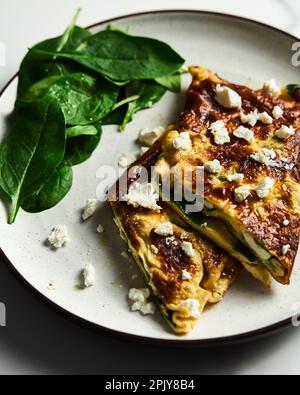 Folded omelette stuffed with spinach and feta on the white plate with spinach leaves on back. Healthy and dietary breakfast dish. Minimalistic food Stock Photo
