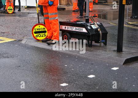 London, United Kingdom - February 01, 2019: Road workers in bright orange visibility uniforms, directing traffic at construction site - detail to wet Stock Photo
