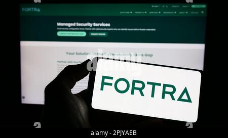Person holding smartphone with logo of US cybersecurity company Fortra LLC on screen in front of website. Focus on phone display. Stock Photo