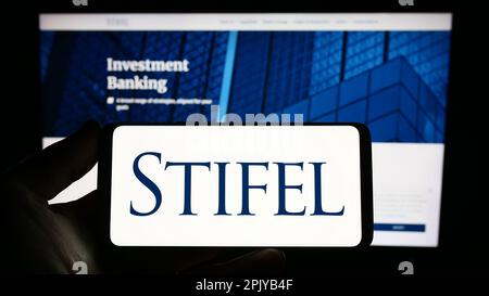 Person holding smartphone with logo of US investment company Stifel Financial Corp. on screen in front of website. Focus on phone display. Stock Photo