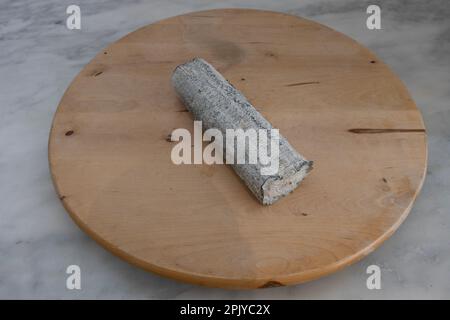 French culinary Still Life. Piece of cheese Sainte Maure De Touraine placed on a wooden pan Stock Photo