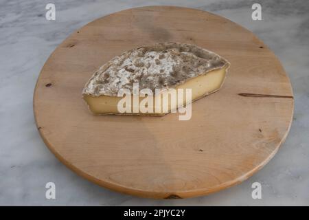 French culinary Still Life. Piece of cheese Tomme de Savoie placed on a wooden pan Stock Photo