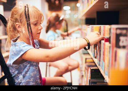 Schoolgirls looking for books in school library. Students choosing books. Elementary education. Doing homework. Learning from books. Back to school Stock Photo