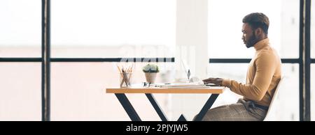 Serious black millennial man typing on laptop, has video call at modern workplace in minimalist office interior Stock Photo