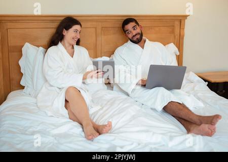 Cheerful Wife Showing Digital Tablet To Husband Sitting In Bedroom Stock Photo