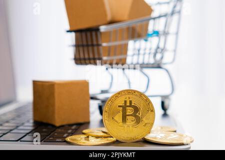 Bitcoin coins on the laptop and a mini toy shopping cart with cardboard boxes on the background. Mining and web banking concept. International network payment.  Stock Photo