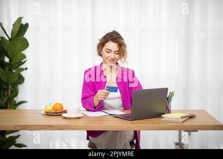 Smiling Young Female Freelancer Using Laptop And Credit Card At Home Office Stock Photo