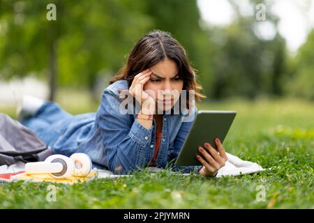 Stressed young arab woman looking at digital tablet screen outdoors and frowning Stock Photo