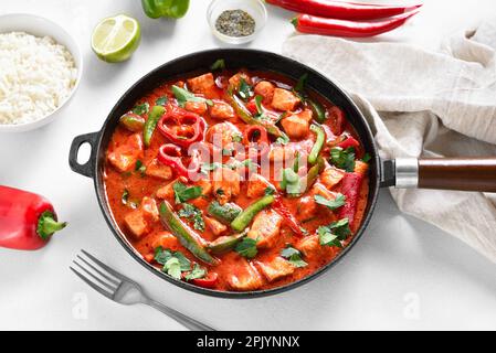 Thai style red chicken curry with vegetables in cast iron pan on white stone background. Close up view Stock Photo