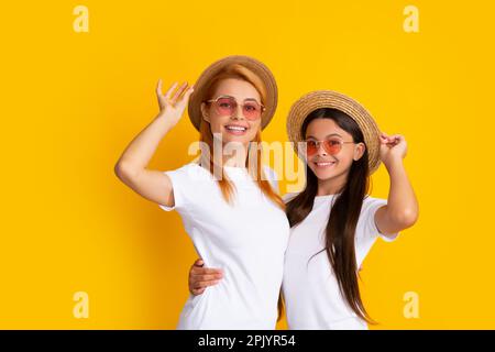 Fashion style. Young mother and teenage girl daughter lovely hugging and cuddling, wearing t-shirt straw hat and sunglasses, isolated on bright yellow Stock Photo