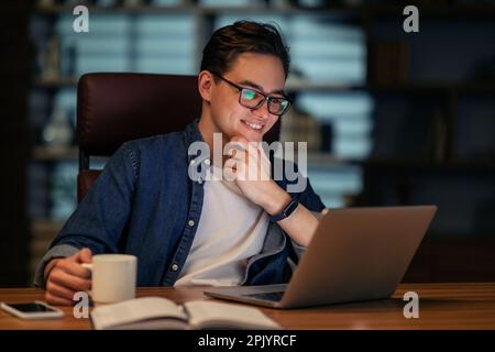 Employee looking at computer screen and smiling, drinking coffee Stock Photo