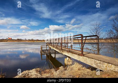 March spring day. Ice and snow melting on lake surface. Clouds reflection in water. Church on hill on background. Calm weather. Season change. Belarus Stock Photo