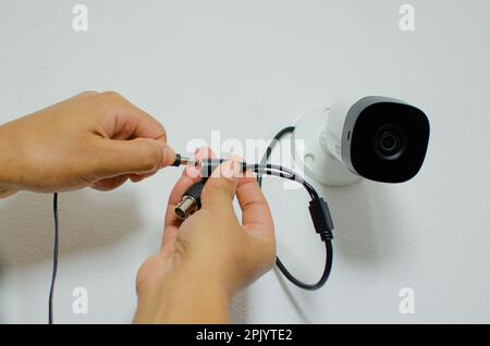 A closeup of hands installing a home security camera, connecting it to a power source Stock Photo
