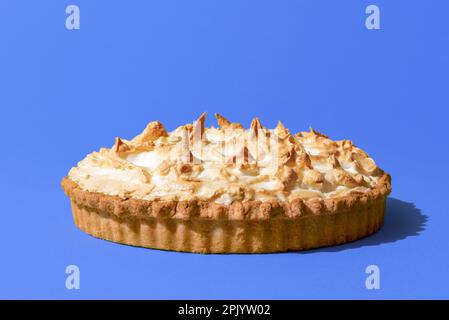 Delicious homemade meringue cake with a lemon flavor filling, minimalist on a blue indigo table. Lemon meringue tart isolated on a vibrant colored bac Stock Photo