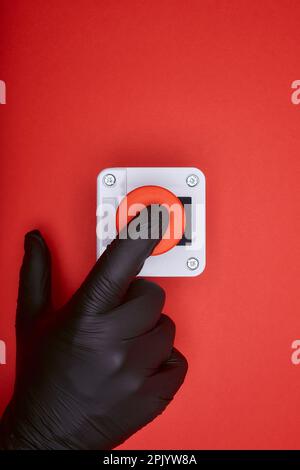 The hand in black vinyl glove, which pushes the emergency button at the red background at the top view Stock Photo