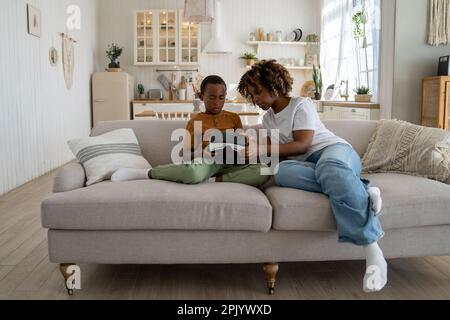 Black woman mom teaching kid son how to use VR headset for learning and education Stock Photo