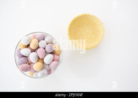 Glass bowl filled with chocolate mini eggs on a white background, shown with yellow cupcake cases (Easter) Stock Photo