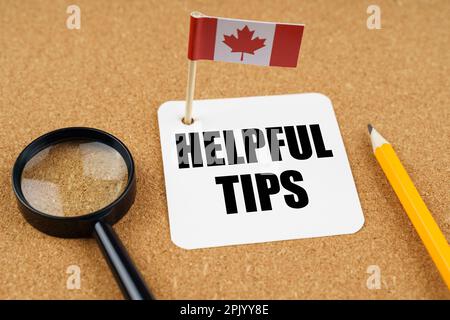 On the table is the flag of Canada, a pencil, a magnifying glass and a sheet of paper with the inscription - Helpful Tips Stock Photo