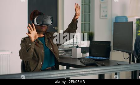 African american developer working with vr glasses to create programming server with html script on terminal window. System engineer using virtual reality headset to plan new interface. Stock Photo