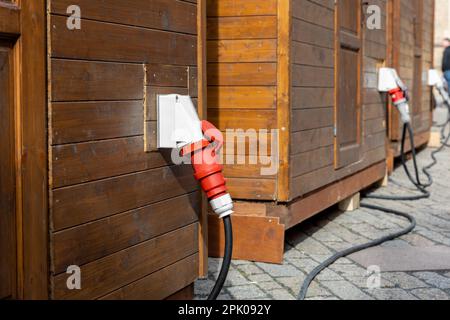Row of small wooden cabins city street with industrial high voltage wall-mounted sockets electric cabel. Temporary energy 380v waterptoof power supply Stock Photo