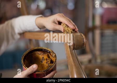 Close up of artisan hand applying wax to old vintage chair in furniture workshop Stock Photo