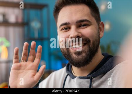 POV of Caucasian man blogger taking selfie on smartphone, communicating video call online with social media subscribers followers, recording vlog stories. Young guy at home apartment room on couch Stock Photo