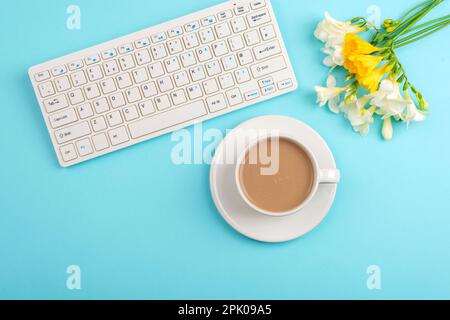 Computer keyboard and coffee cup on turquoise table with freesia flowers. Top view, flat lay, copy space. Stock Photo