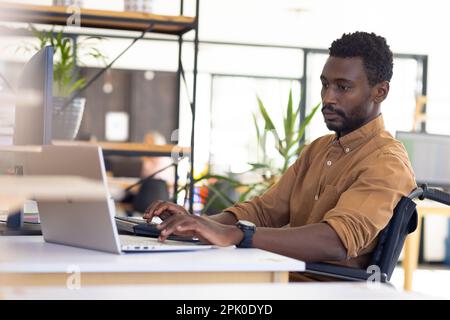 Disabled casual african american businessman in wheelchair using computer in modern office Stock Photo