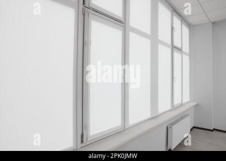 Window with closed white roller blinds indoors Stock Photo