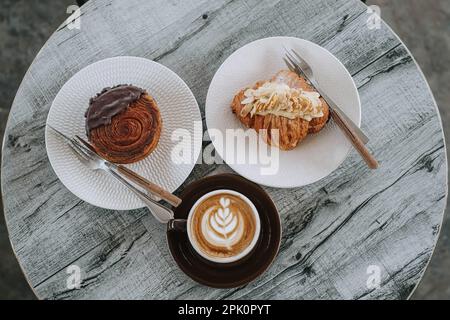 Breakfast Set: Almond Croissant, Chocolate Crombolomi, and a Cup of Coffee on Wooden Table. Flat Lay. Stock Photo