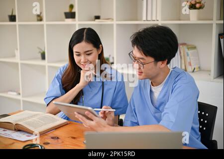 Two smart young Asian medical students are using digital tablet, preparing for exams, and studying together in a library. Stock Photo