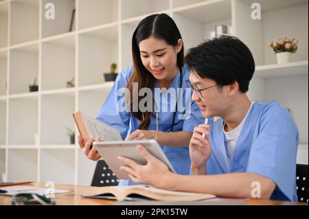 Two smart and focused young Asian medical students in uniform are discussing and researching medical information in a library together. Stock Photo