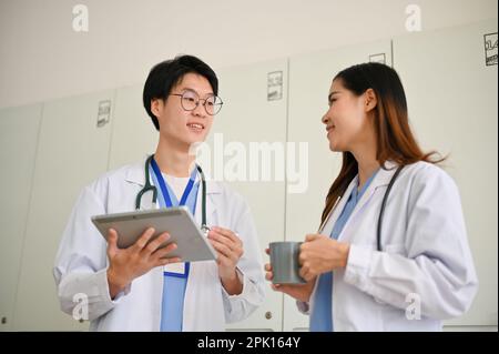 Smart and handsome young Asian male doctor or medical student discussing his medical cases with a female colleague during the coffee break. Stock Photo