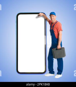 Repair service - just call. Happy professional repairman holding toolbox and smartphone with blank screen on light blue background, space for design Stock Photo