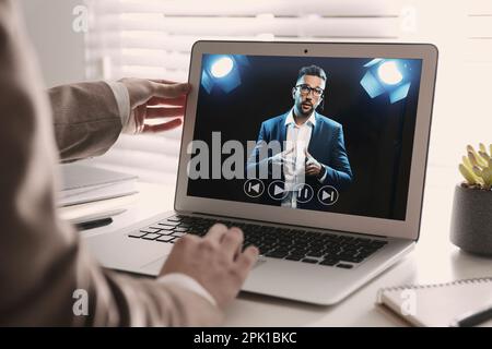 Woman watching performance of motivational speaker on laptop at white table, closeup Stock Photo