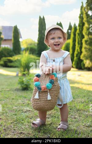 Cute little girl in stylish clothes with knitted backpack outdoors on sunny day Stock Photo
