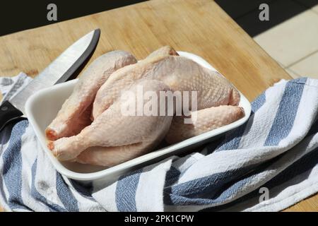 Fresh raw whole chicken in plastic container, knife and napkin on wooden table Stock Photo