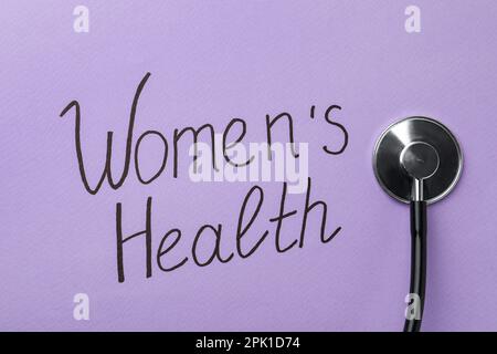 Stethoscope near text Women's Health on violet background, top view Stock Photo