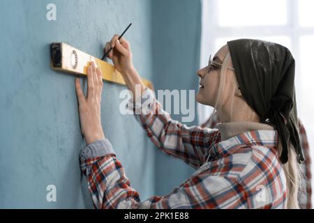 Side view of couple doing house renovation together. Woman and her boyfriend using measurement level redecorating apartment Stock Photo
