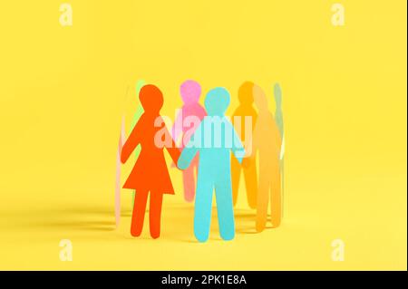 Many different paper human figures standing in circle on yellow background. Diversity and inclusion concept Stock Photo