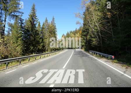 Asphalt road with word Start surrounded by forest on sunny day Stock Photo