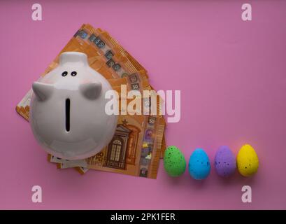 Piggy bank surrounded by colorful Easter eggs on pink background. Stock Photo