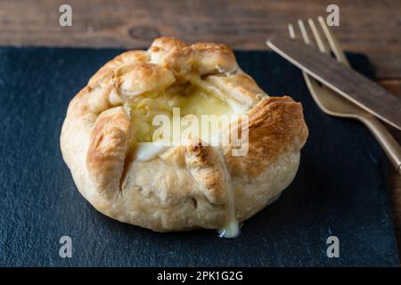 Camembert cheese baked in puff pastry with a fork and knife, close up Stock Photo