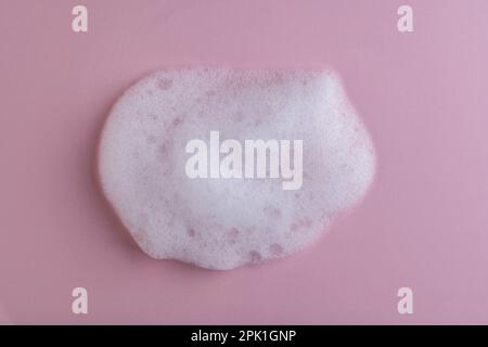 White cleanser foam bubbles on pink background or texture, close up, top view. Soap suds or foam and bubbles from detergent or shower gel or shampoo Stock Photo